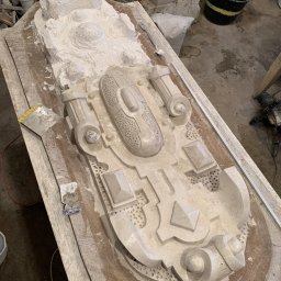 SZTUKATORSTWO Robert Zimmer - Gipsowy odlew dekoracyjnego elementu architektonicznego na drewnianym stole warsztatowym, widoczne narzędzia i resztki gipsu.