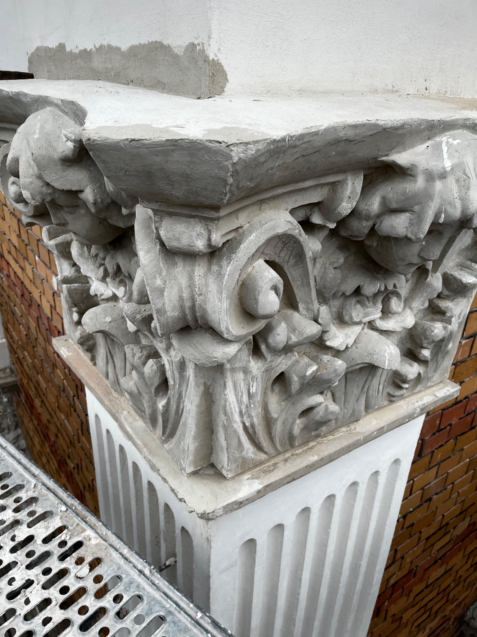Detal kolumny z dekoracyjnym kapitelem w trakcie prac renowacyjnych, widoczne rusztowanie i fragment ceglanej ściany.