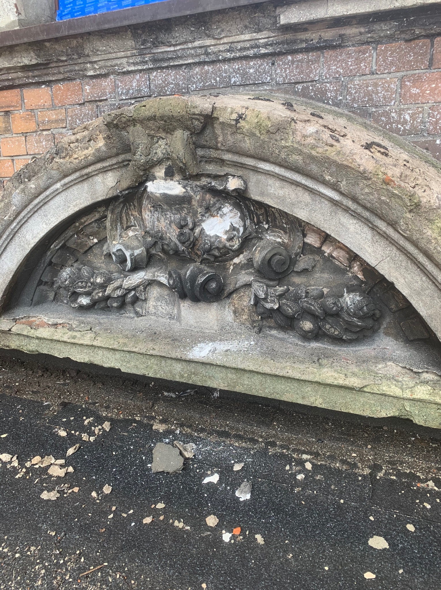 Zniszczony, kamienny naddzwierek z dekoracyjnymi płaskorzeźbami, fragment elewacji budynku z cegły.