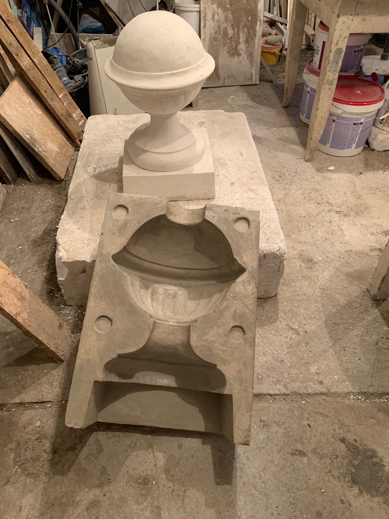 Gipsowa forma i gotowy element dekoracyjny w kształcie kuli na cokole, widoczne materiały i narzędzia w warsztacie.