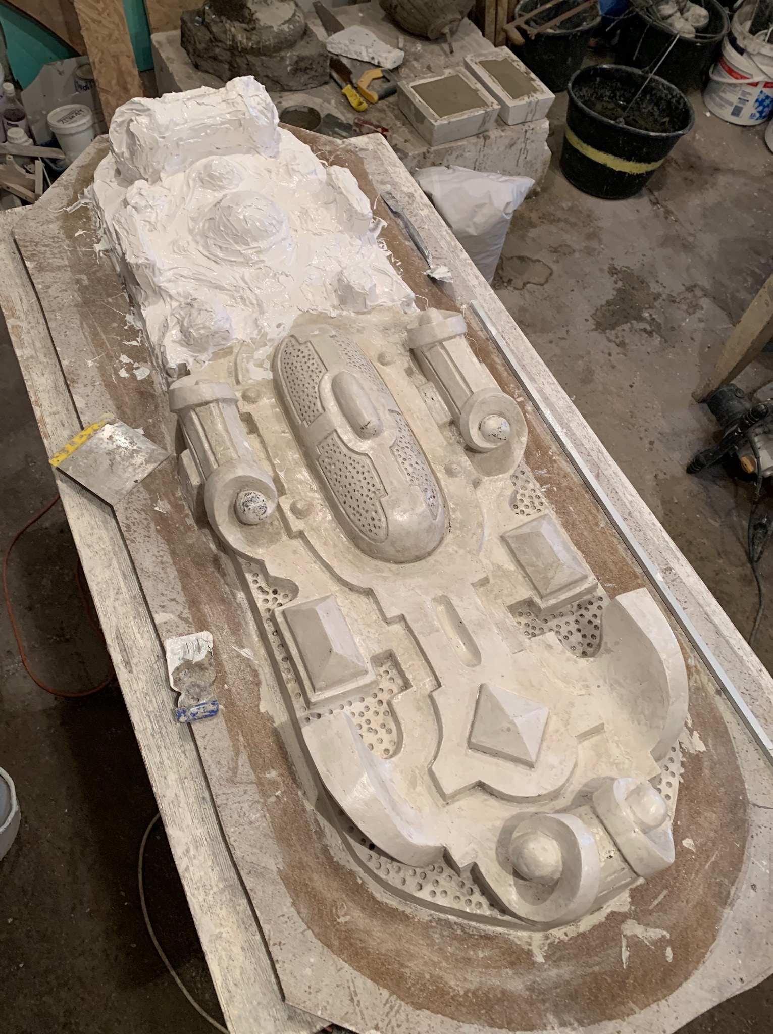 Gipsowy odlew dekoracyjnego elementu architektonicznego na drewnianym stole warsztatowym, widoczne narzędzia i resztki gipsu.