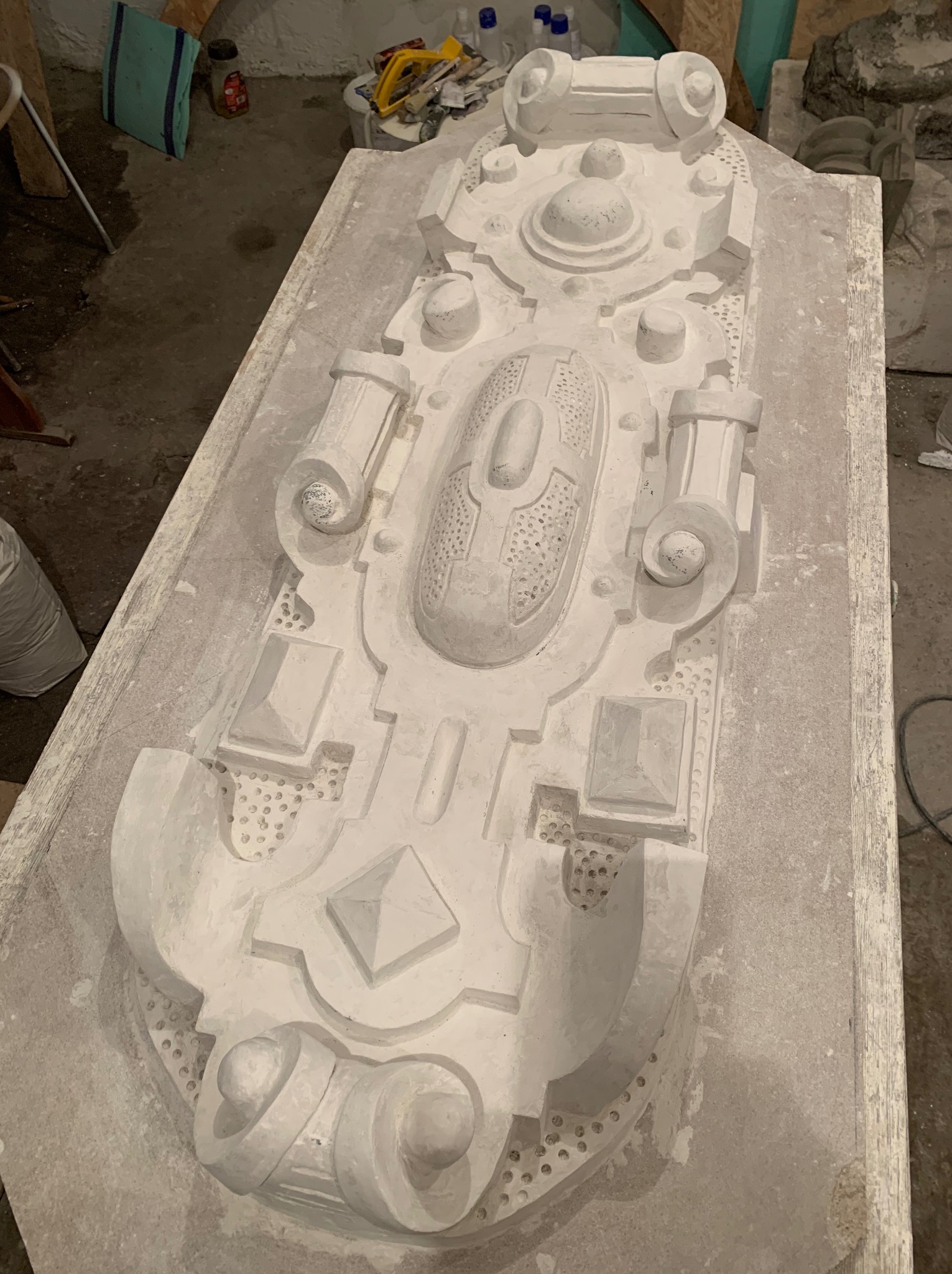 Gipsowy odlew dekoracyjnego elementu architektonicznego na drewnianym stole, prawdopodobnie fragmentu elewacji, w trakcie prac konserwatorskich.