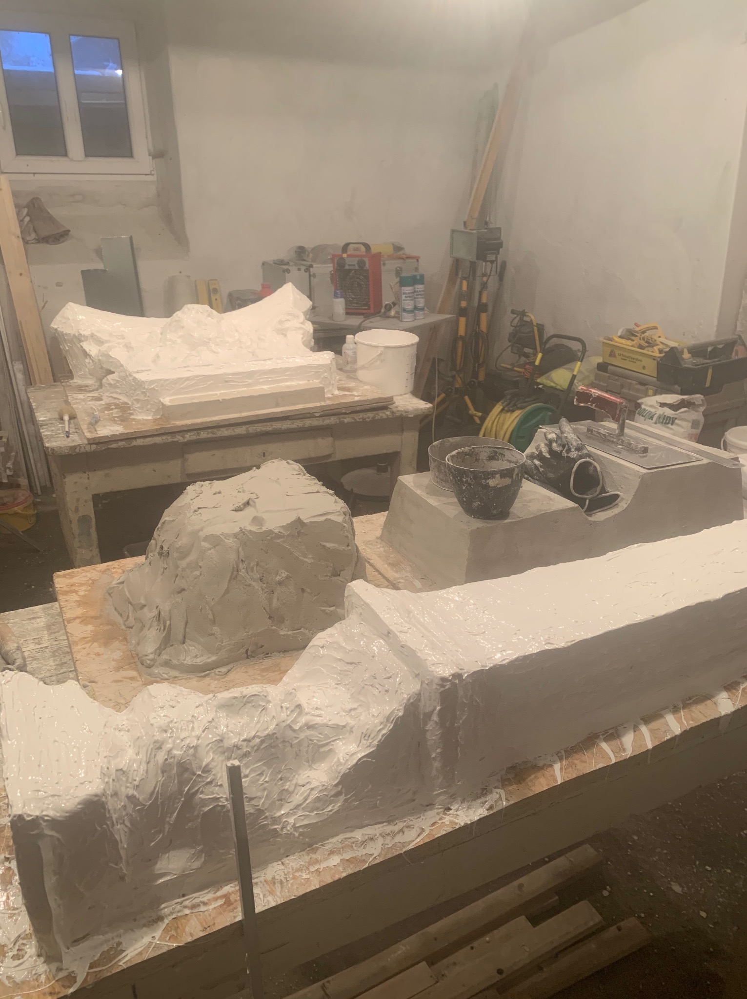 Pracownia z elementami dekoracyjnymi elewacji w trakcie tworzenia, pokryte świeżą warstwą białej zaprawy. W tle widoczne narzędzia i materiały budowlane.