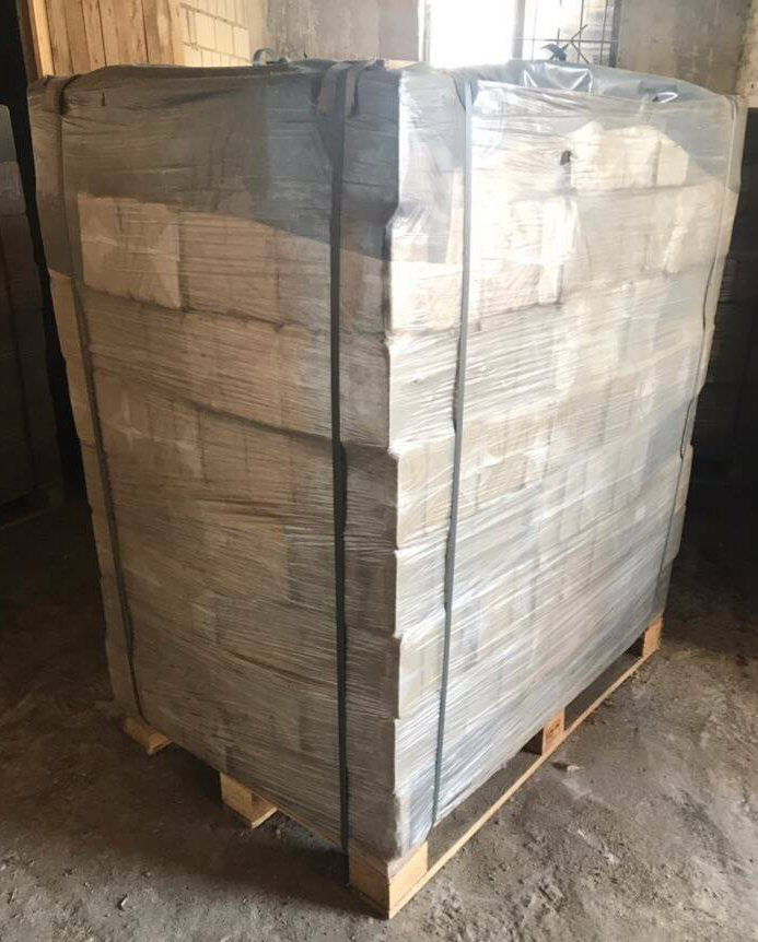 Paleta z kostkami opału owinięta folią i zabezpieczona taśmami, widoczna w magazynie z betonową podłogą.