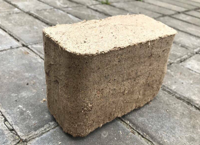 Prostopadłościenny blok sprasowanych trocin na szarej kostce brukowej, widoczne drobne włókna drzewne.