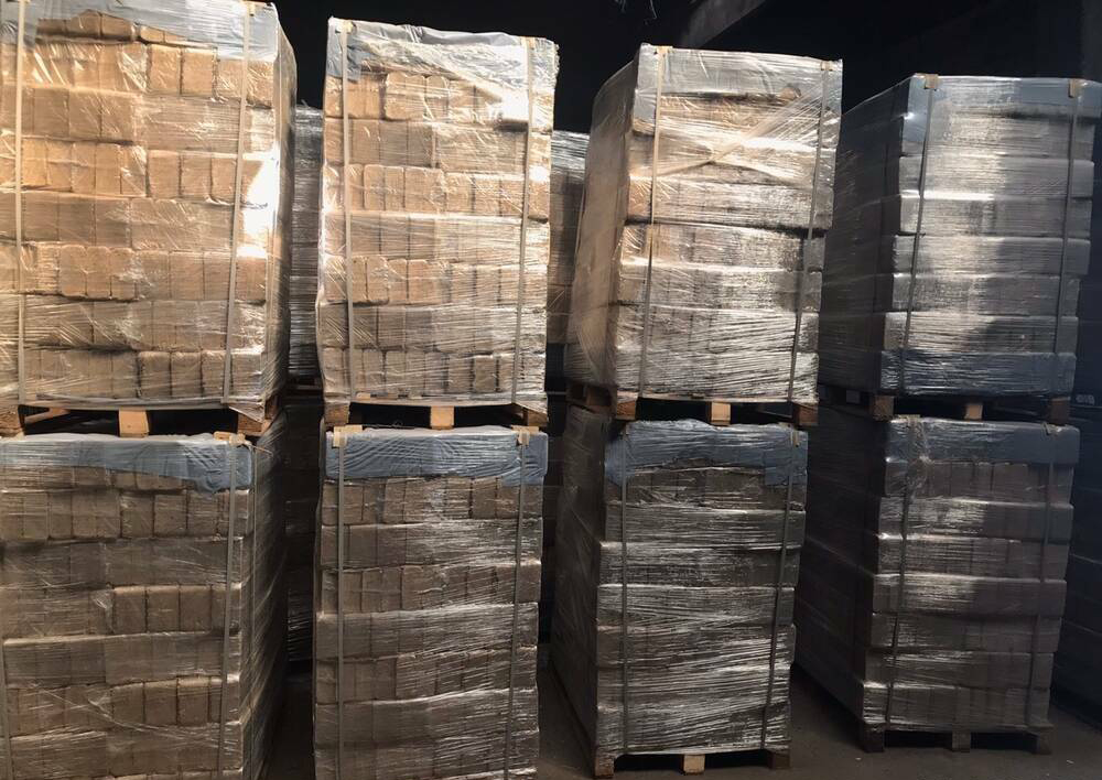 Ułożone na paletach, owinięte folią pakiety z kostkami opału drzewnego, w magazynie.