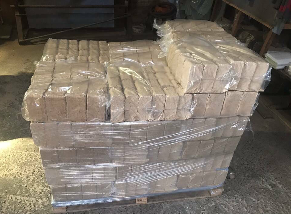 Paleta z ułożonymi warstwami kostek materiału opałowego, częściowo owiniętych folią, w magazynie.