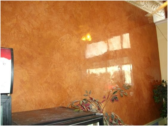 Ściana w odcieniach brązu z efektem dekoracyjnym, odbijająca światło okien, z rośliną doniczkową w rogu.