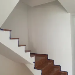 Klatka schodowa w trakcie malowania na biało, zabezpieczona taśmą malarską na brzegach stopni wyłożonych terakotą, widoczne ślady po wcześniejszych pracach remontowych.