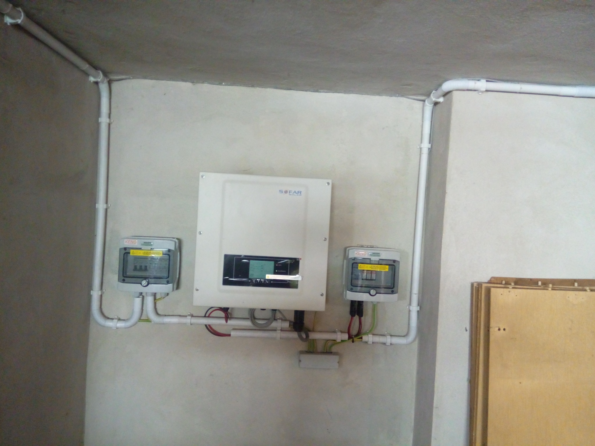 Biała skrzynka SOFAR z wyświetlaczem i dwa liczniki KENO w szarych obudowach, zamontowane na ścianie z widocznymi rurami instalacyjnymi.