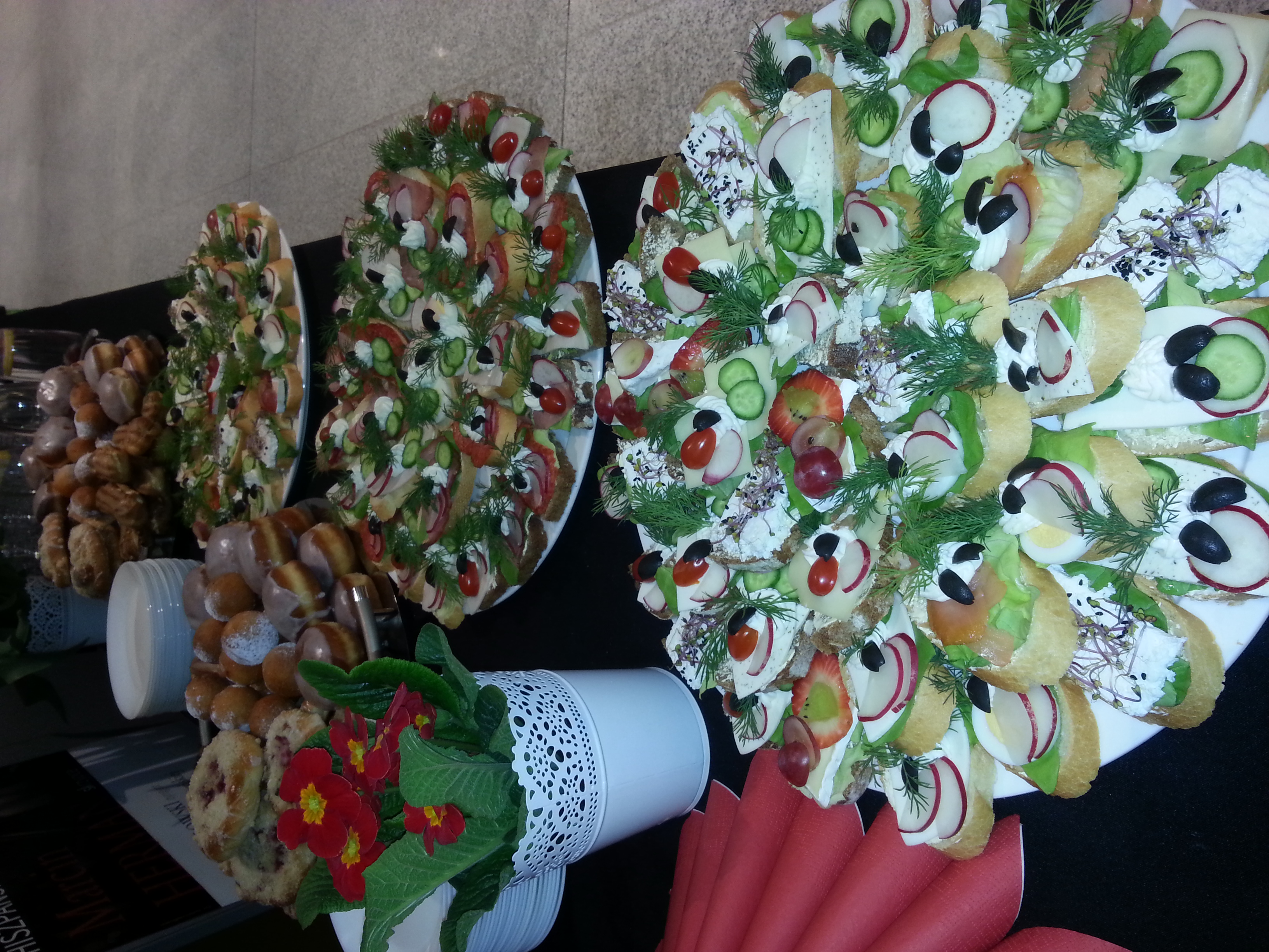 Dekoracyjne patery z kanapkami i słodkimi przekąskami, przygotowane przez firmę z Poznania, z bliska widoczne świeże warzywa i zioła.