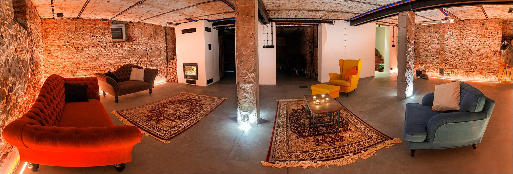 Rustykalne wnętrze z ceglanymi ścianami, oświetleniem LED, kominkiem, dywanami orientalnymi i różnokolorowymi sofami, zaaranżowane na potrzeby imprezy lub sesji zdjęciowej.