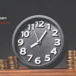 Czarny zegar wskazujący godzinę 7:58, ustawiony obok trzech stosów złotych monet na drewnianym biurku, w tle logo firmy rachunkowej.