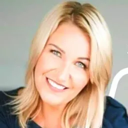 Uśmiechnięta blondynka z niebieskimi oczami, delikatny makijaż, włosy opadające na ramię, patrzy w obiektyw.