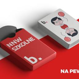 Katarzyna Jońska-Boligłowa - Czerwone pudełko z napisem 'NNW SZKOLNE b.' obok stosu kart z rysunkiem dziecka z balonami, na dwukolorowym czerwono-białym tle.