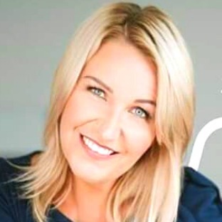 Uśmiechnięta blondynka z niebieskimi oczami, delikatny makijaż, włosy opadające na ramię, patrzy w obiektyw.