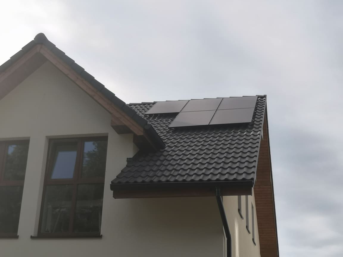 Cztery panele słoneczne na ciemnym, spadzistym dachu domu jednorodzinnego z brązowymi oknami i kremową elewacją, widoczne rynny.