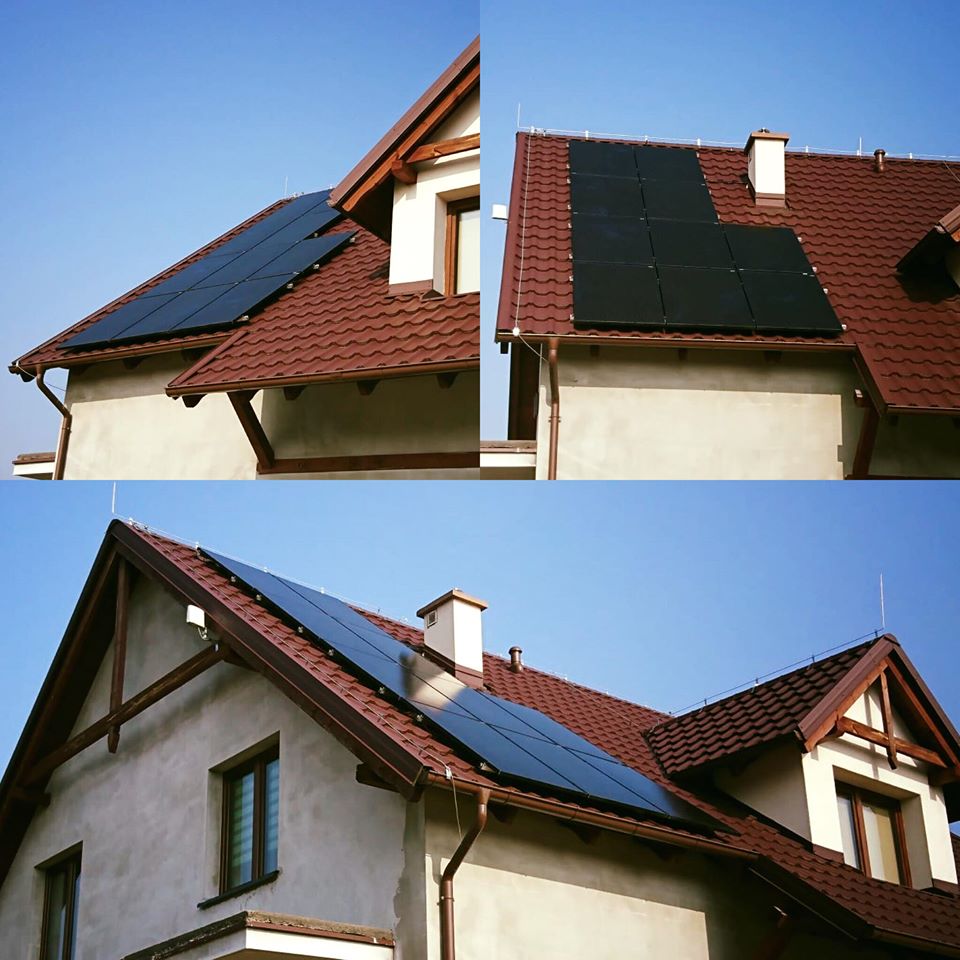 Panele słoneczne na dachu domu jednorodzinnego z brązową dachówką, widoczne okna i komin, błękitne niebo w tle.