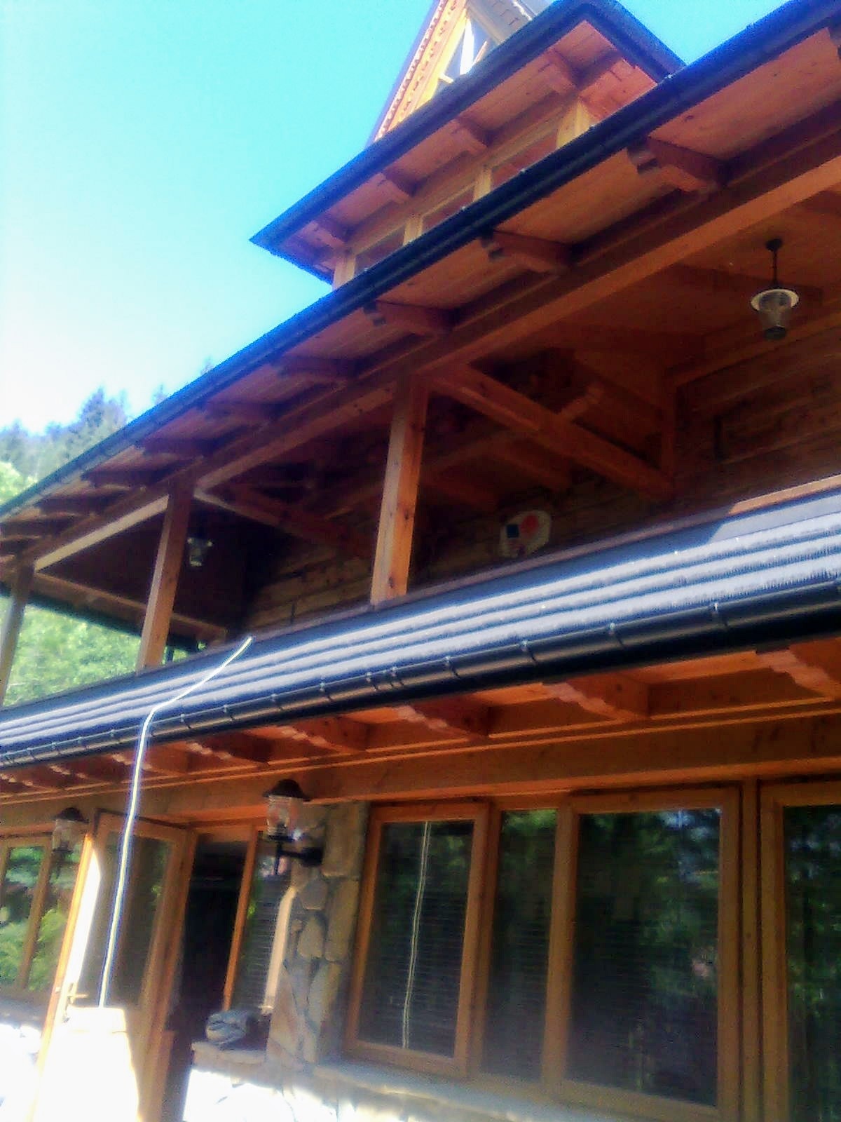 Dwupiętrowy dom z bali z drewnianą konstrukcją szkieletową, czarnymi rynnami i kamiennymi elementami elewacji, widziany z dołu pod kątem.