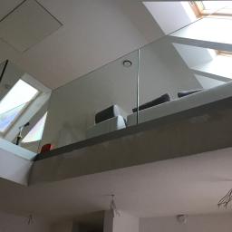 FrezDruk - Szklana balustrada na antresoli z widokiem na okna dachowe i fragment sofy. Balustrada zamontowana na szarej konstrukcji.