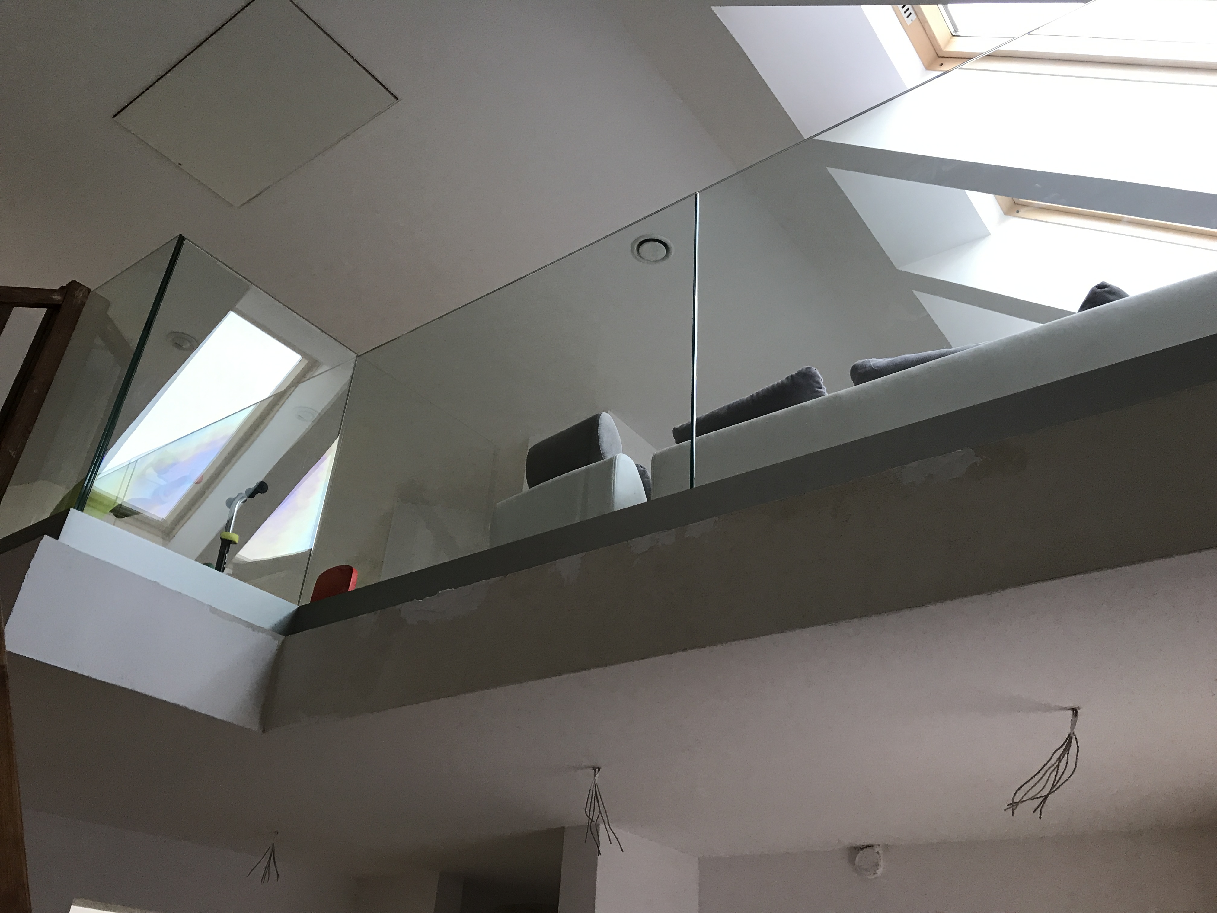 Szklana balustrada na antresoli z widokiem na okna dachowe i fragment sofy. Balustrada zamontowana na szarej konstrukcji.