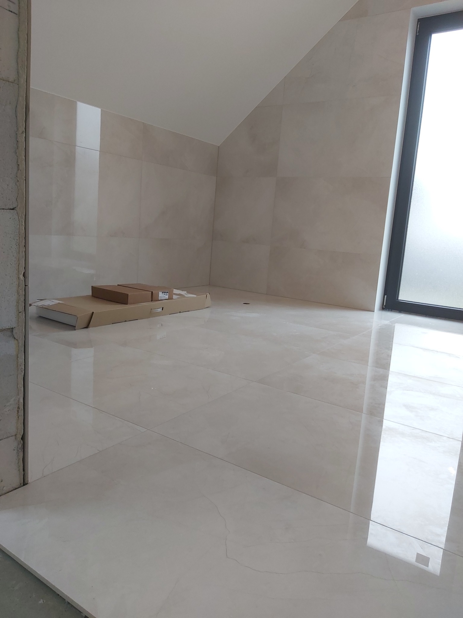 Jasne, błyszczące płytki ceramiczne na podłodze i ścianach w łazience w trakcie remontu, z kartonami płytek w rogu oraz widocznym oknem.