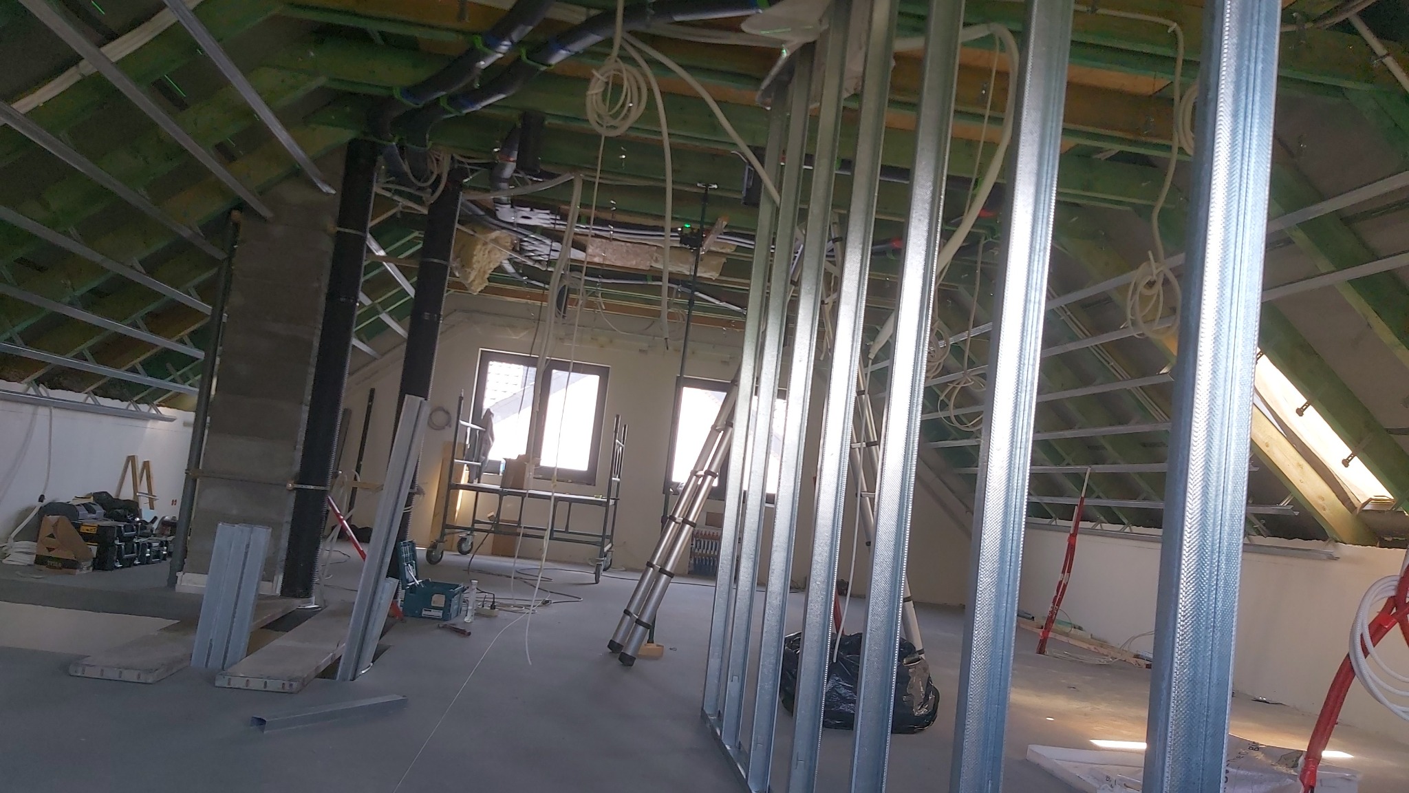 Montaż metalowej konstrukcji szkieletowej pod płyty gipsowo-kartonowe na poddaszu, widoczne profile, narzędzia, instalacje pod sufitem, okna dachowe.