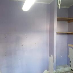 Fach-Nid - Pokój w trakcie remontu: ściany pomalowane na fioletowo, widoczne ślady po szpachlowaniu, drewniane półki, drabina malarska w rogu, lampa sufitowa i fragment instalacji hydraulicznej.