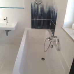 Nowoczesna łazienka z białą wanną, umywalką i płytkami z motywem miasta w tle, chromowana armatura.