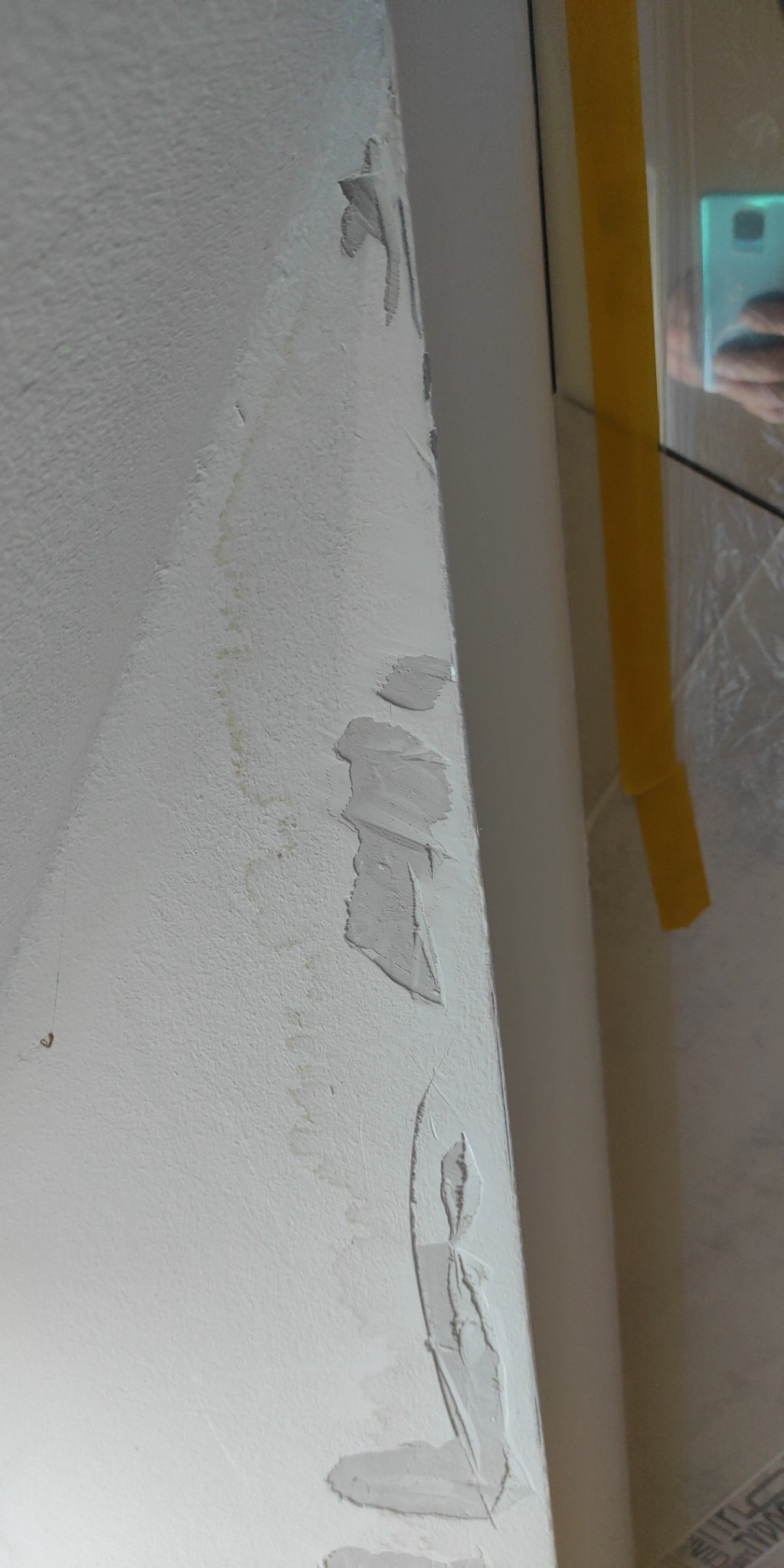 Ściana z nałożoną, ale jeszcze nie wyschniętą warstwą szpachli, widoczne fragmenty żółtej taśmy malarskiej przy framudze okna.