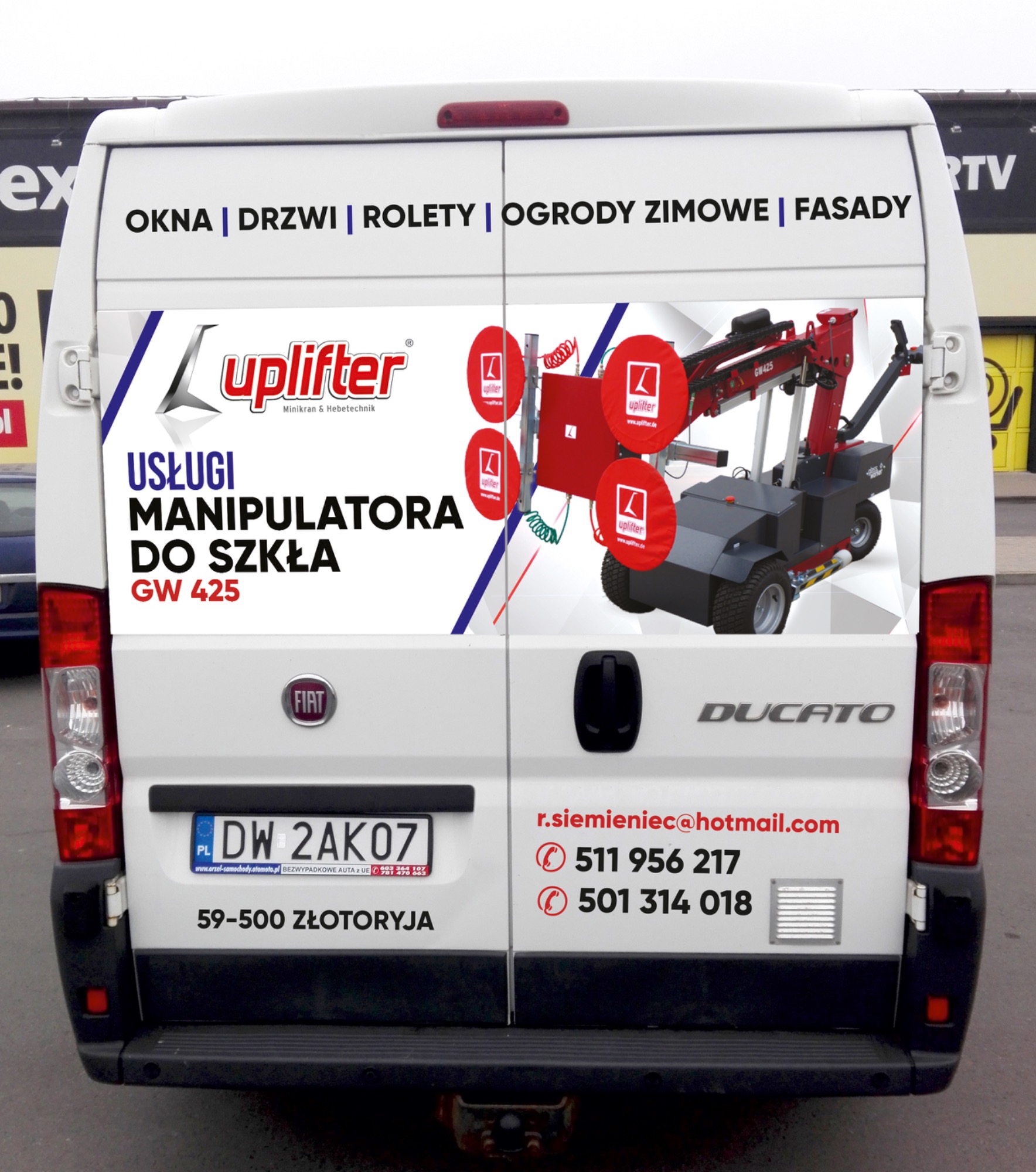 Tył białego samochodu dostawczego Fiat Ducato z reklamą usług montażu okien, drzwi i rolet na terenie Złotoryi, oferowanych przez firmę Uplifter, specjalizującą się w manipulacji szkłem za pomocą...