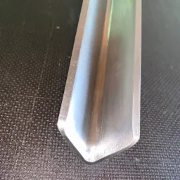 Błyszczący, metalowy element obrobiony na tokarce leży na ciemnej, teksturowanej powierzchni, widoczne delikatne refleksy świetlne.