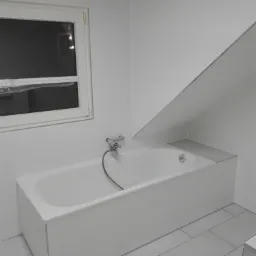 Biała wanna w łazience na poddaszu, wykończona białymi płytkami, z oknem zabezpieczonym folią, szara armatura.