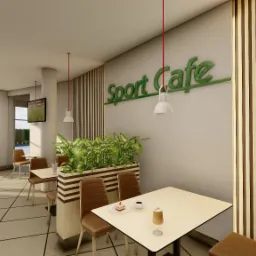 Wnętrze kawiarni sportowej z jasnymi ścianami, drewnianymi akcentami, roślinami w donicach i telewizorem wyświetlającym mecz piłki nożnej. Na stołach kawa i ciasto.