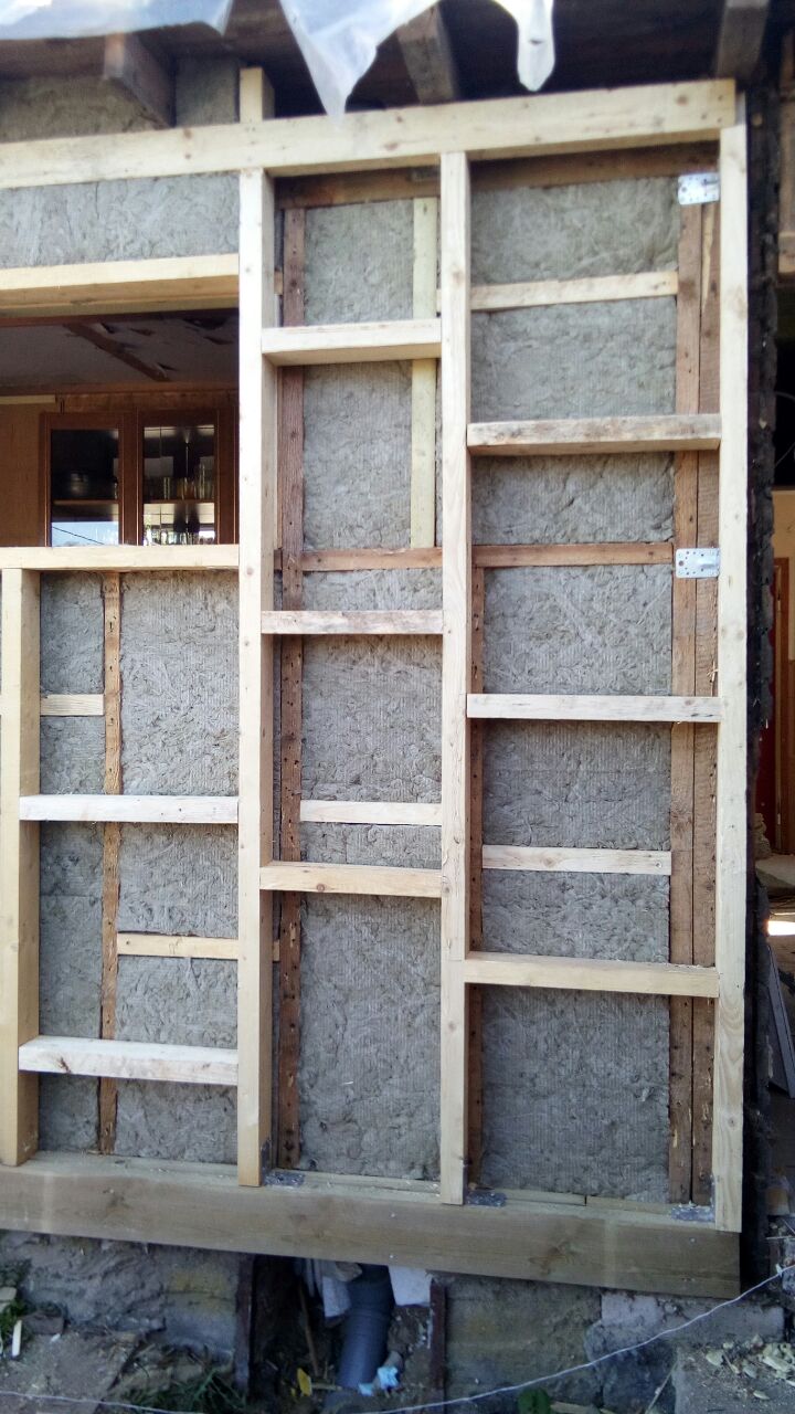 Ocieplenie ściany budynku wełną mineralną, widoczna drewniana konstrukcja szkieletowa, okno w tle.