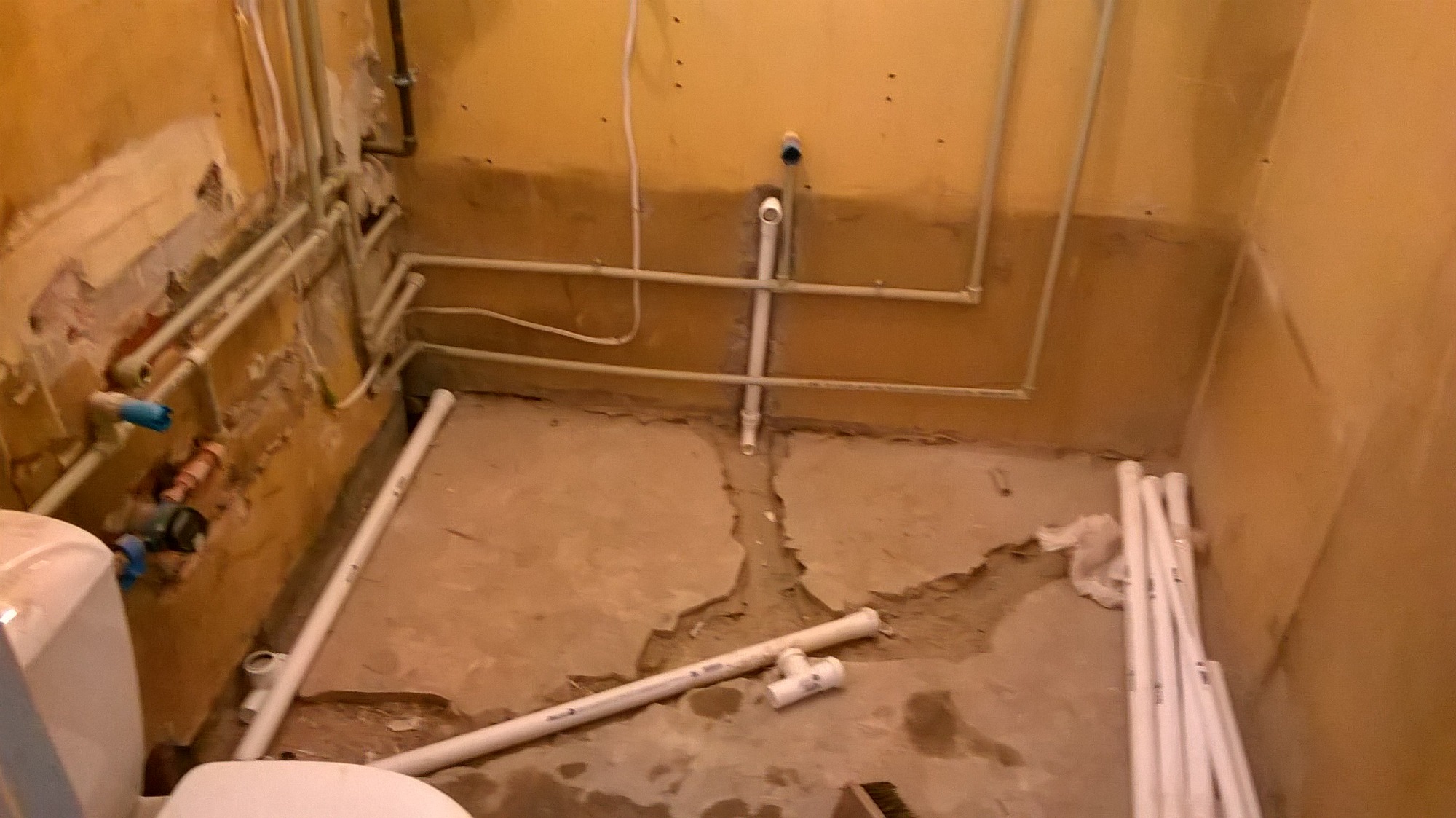 Łazienka w trakcie remontu: widoczne rury hydrauliczne, częściowo usunięte płytki i przygotowane do montażu nowe rury PCV.