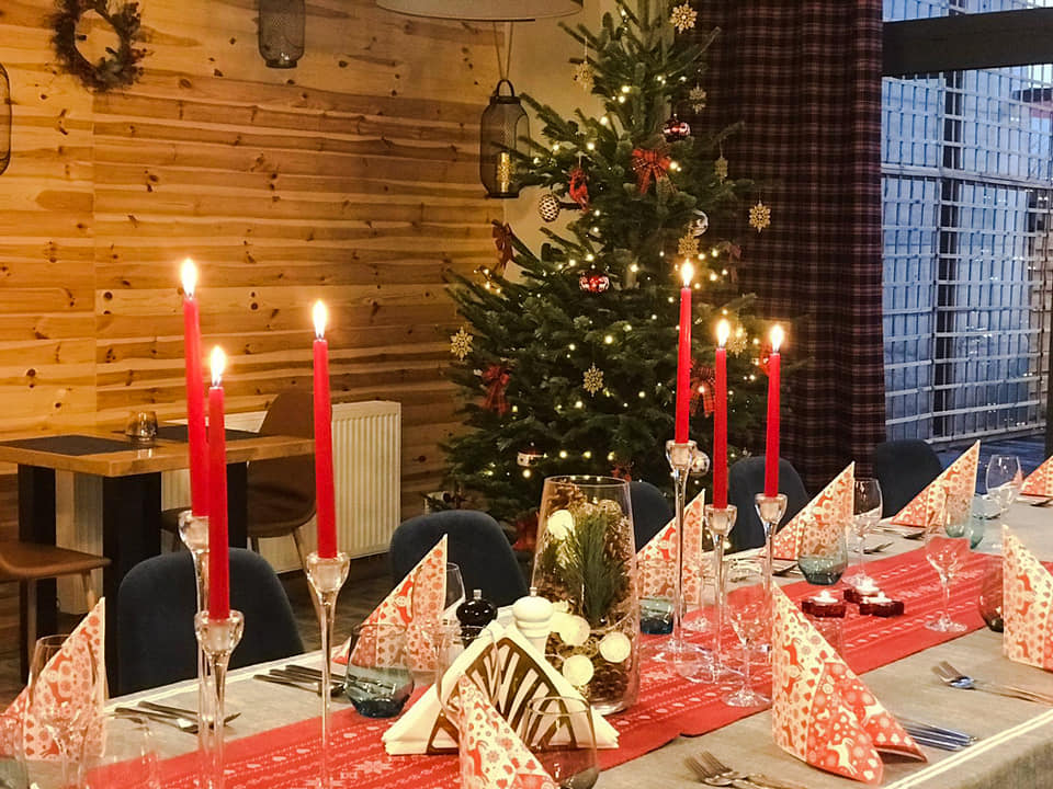 Świątecznie udekorowany stół w Dąbrowie Górniczej z płonącymi czerwonymi świecami w kryształowych świecznikach, wzorzystymi serwetkami, bieżnikiem z motywem świątecznym i choinką w tle.