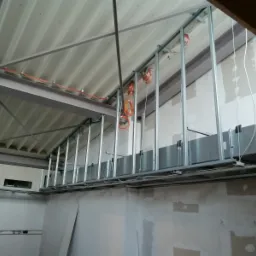 Metalowa konstrukcja szkieletowa sufitu podwieszanego z widocznymi przewodami elektrycznymi i fragmentami wentylacji, przed montażem okładzin.