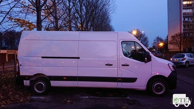 Biały samochód dostawczy Renault Master zaparkowany na poboczu w jesienny wieczór, widoczny budynek mieszkalny w tle.