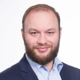 Portret mężczyzny z brodą w niebieskiej koszuli i marynarce na białym tle.