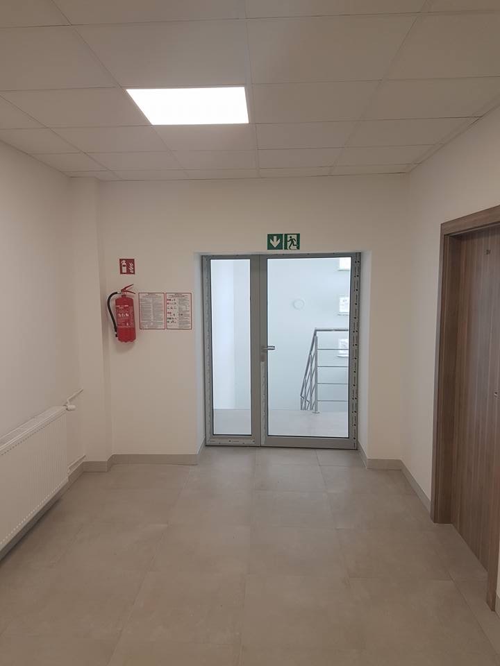 Korytarz biurowy z oznakowaniem ewakuacyjnym, gaśnicą i drzwiami przeciwpożarowymi