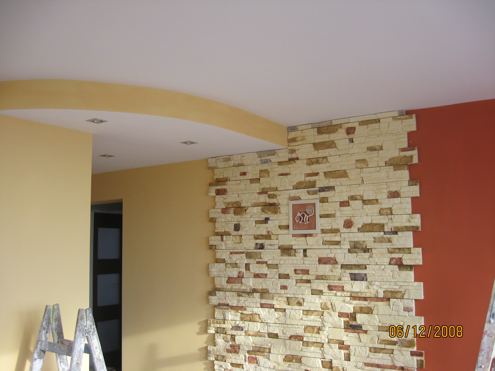 Wykończone wnętrze z dekoracyjną ścianą z kamienia, żółtymi ścianami, pomarańczowym fragmentem ściany i schodami malarskimi w rogu.