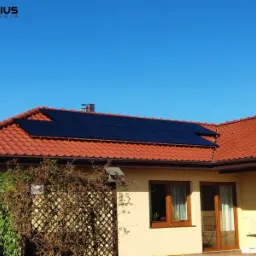 Czerwony dach z dachówki ceramicznej z instalacją paneli słonecznych, widok z poziomu ogrodu, błękitne niebo w tle, logo firmy w lewym górnym rogu.