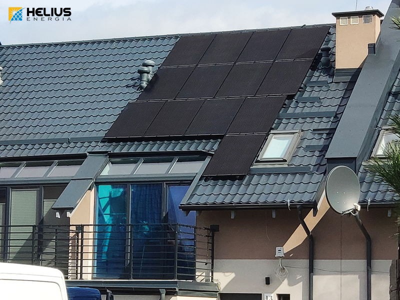 Panel słoneczny zintegrowany z szarym dachem domu jednorodzinnego z widocznym balkonem i anteną satelitarną.