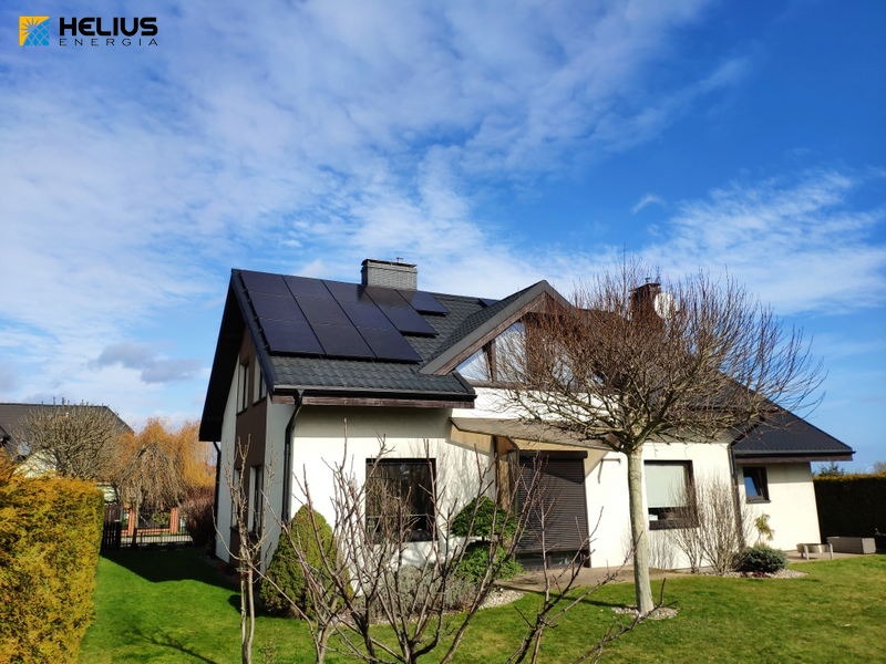 Biały dom jednorodzinny z ciemnymi panelami słonecznymi na dachu, widok z poziomu ogrodu w słoneczny dzień.