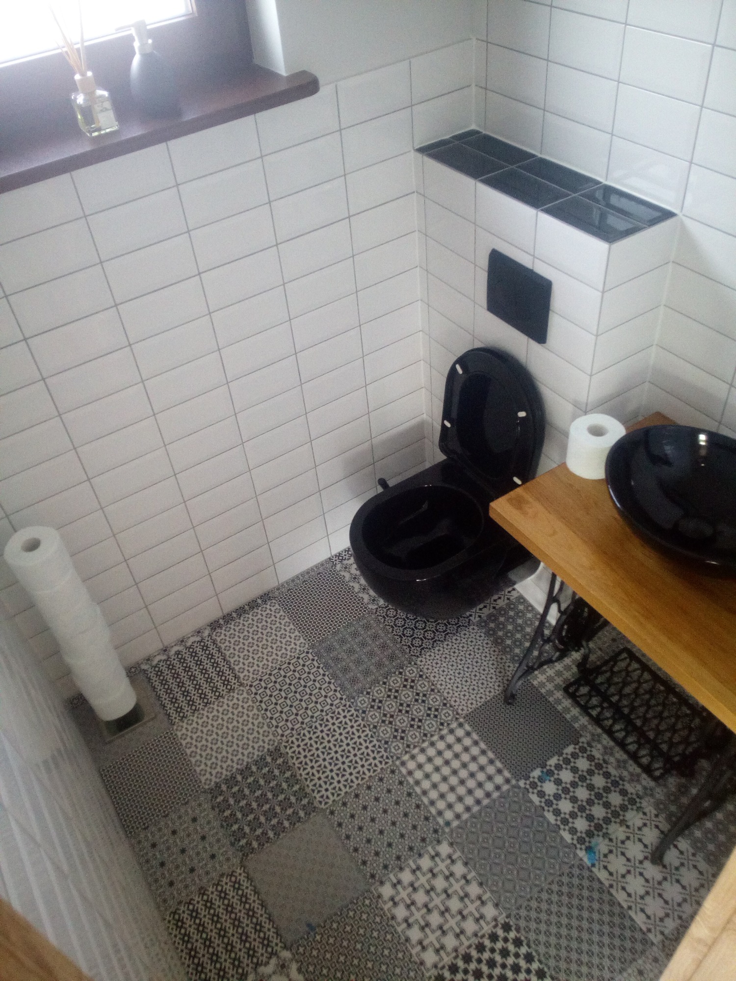 Wykończona łazienka z czarną armaturą, białe płytki na ścianach i patchworkowa podłoga.