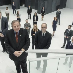 Grupowe zdjęcie zespołu prawniczego w garniturach, z perspektywy z góry, na białym tle nowoczesnego biura z minimalistycznym designem.