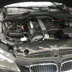 Otwarta maska czarnego samochodu, widoczny silnik z instalacją LPG, z przewodami i reduktorem w kolorze czerwonym.