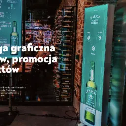 Dwa rodzaje materiał&oacute;w promocyjnych w Gdańsku: podświetlany pionowy baner Jameson Caskmates IPA Edition oraz plakat na tle restauracji Hala Koszyki.