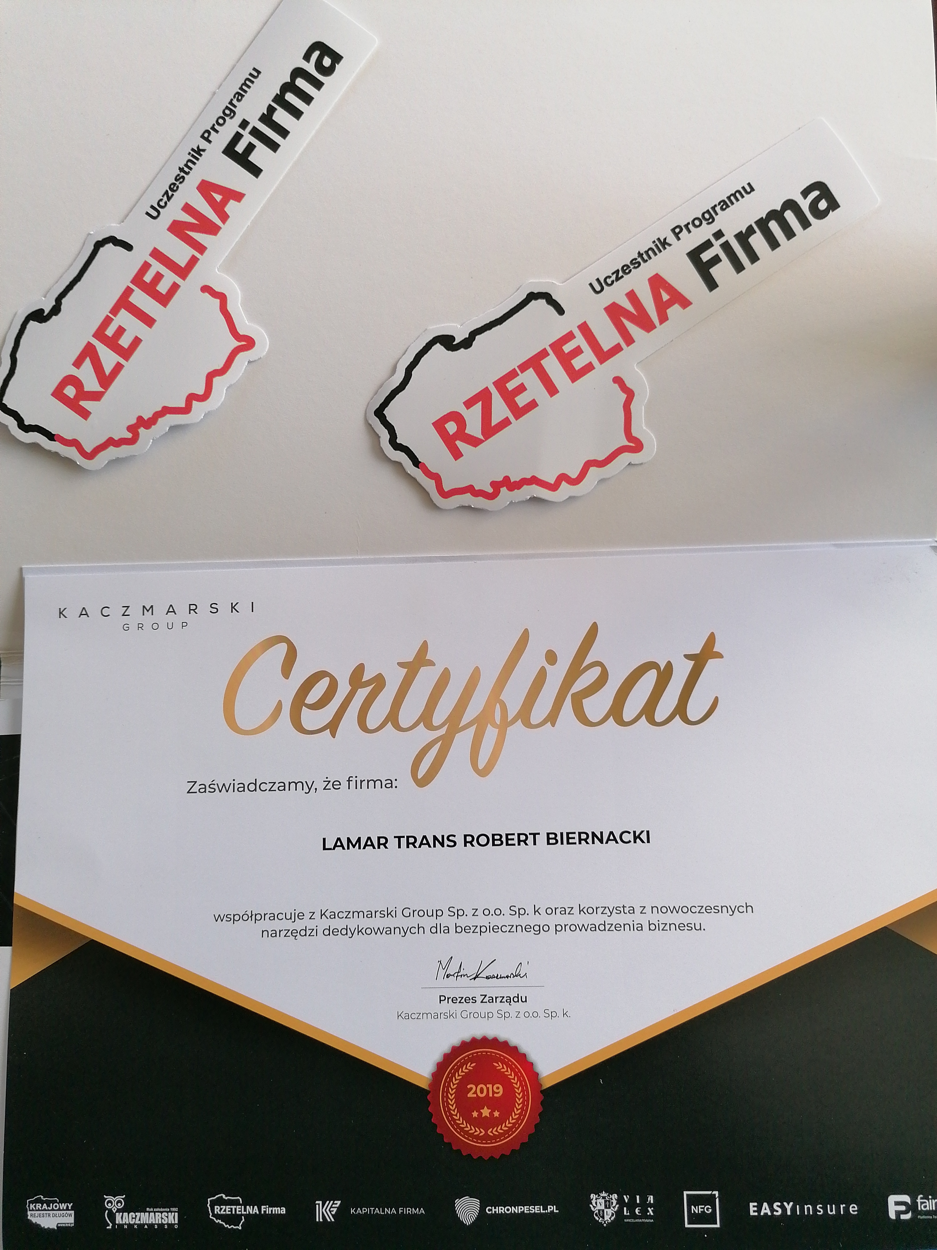 Certyfikat 'Rzetelna Firma' dla firmy LAMAR TRANS ROBERT BIERNACKI, z naklejkami programu na białym tle.